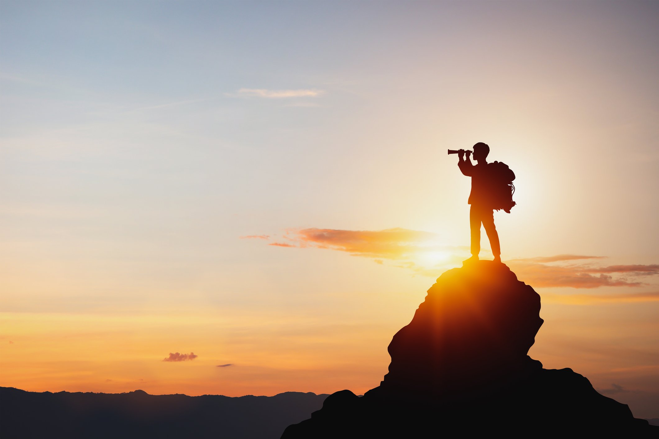 Photo of someone standing on a rock looking off to the left using binoculars