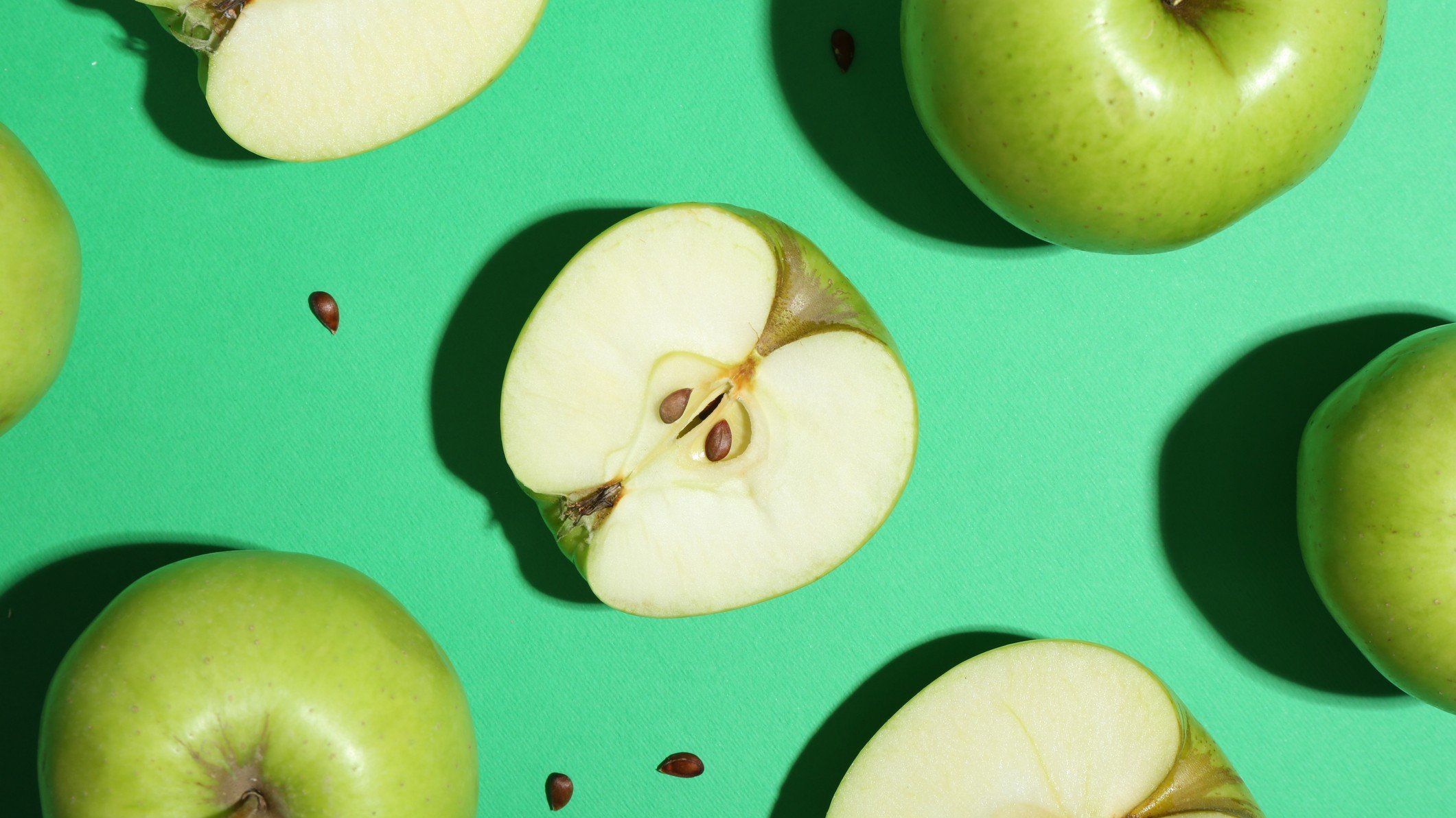 Flat lay composition with whole cut apples and seeds on green background