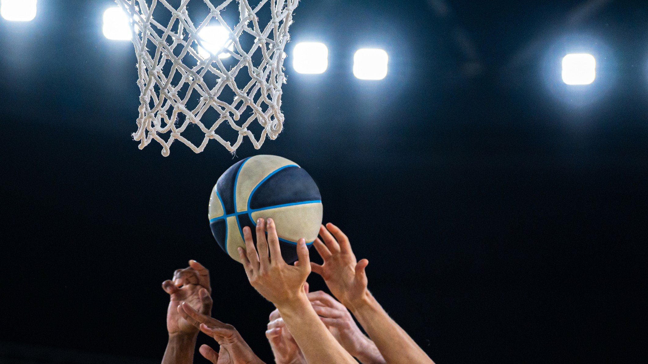 Basketball players hands reaching for a ball near the hoop during a professional game
